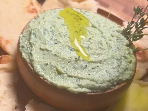 Green herb and cheese spread in terra cotta bowl, topped with olive oil swirl and fresh herb sprig